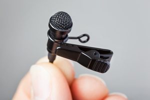 Close-up of a hand holding a tie-clip microphone with a plain background