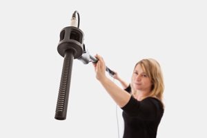 Woman holding a microphone boom against a plain background. Selective focus on the microphone and microphone mount.