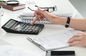 person performing calculations on a calculator on a table with notepads and glasses