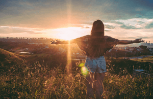 A woman standing on a hill overlooking a city, with her arms outstretched